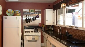 A compact kitchen with a refrigerator, stove, and hanging pots. - Fabulous Downtown Living, 1 BR/1 BA  (Santa Barbara)