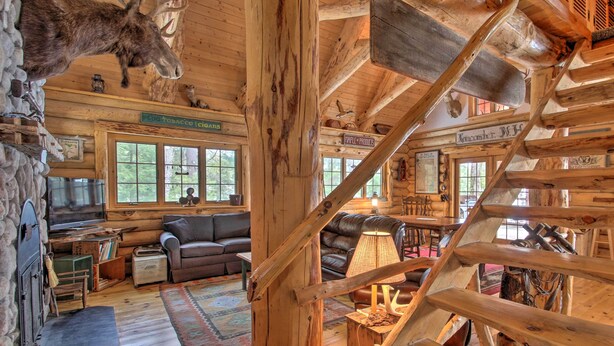 A rustic cabin interior with wooden walls, a fireplace, leather sofas, and a wooden staircase. - Waterfront Conway Vacation Rental w/ Deck! (Conway)