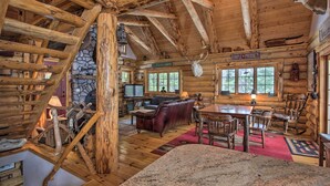 A rustic cabin interior with a stone fireplace, wooden beams, a stone wall, a bar area, and a dining table. - Waterfront Conway Vacation Rental w/ Deck! (Conway)