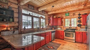 A log cabin kitchen with granite countertops, red cabinets, a large island, and a wood floor. - Waterfront Conway Vacation Rental w/ Deck! (Conway)