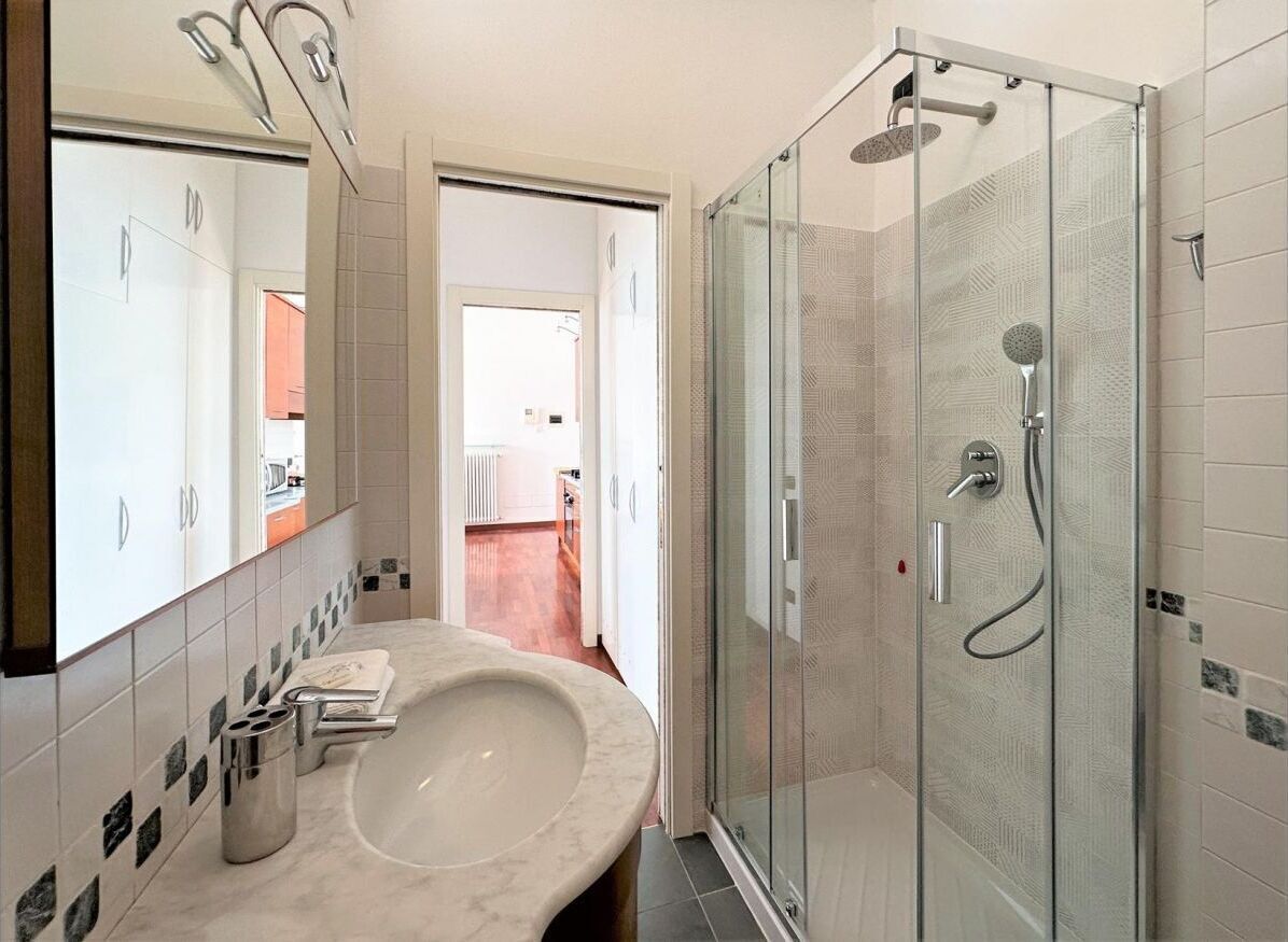 A modern bathroom with a glass-enclosed shower, a large sink, and a mirror.