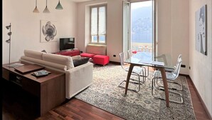 A modern living room with a sofa, a coffee table, a TV, and a dining area with a glass table and chairs. - Larius Apartment Carate Urio (Carate Urio)