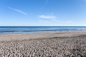 Une plage de sable où l’on peut voir des empreintes menant à l’eau, un ciel dégagé et des vagues douces.