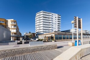 Une zone urbaine côtière comprenant un immeuble moderne de grande hauteur, un restaurant situé au bord de l’eau et une promenade piétonne.