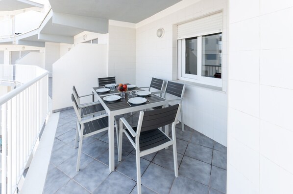 A balcony with a dining table set for four, surrounded by chairs, and a window with blinds.
