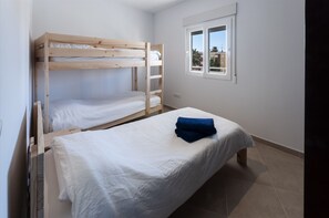 Une chambre avec un lit superposé et un lit simple, tous deux dotés de draps blancs.