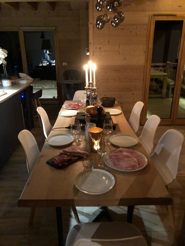Una mesa de comedor con platos, vasos y velas, rodeada de sillas blancas en una habitación de madera.