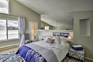 Quarto com uma cama grande, uma cadeira, uma mesa de cabeceira e uma janela com cortinas.