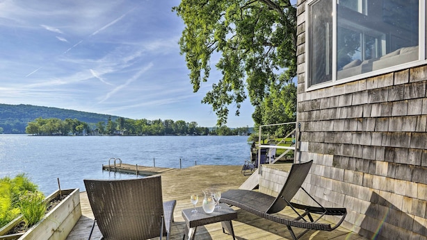 A wooden deck with wicker chairs and a table, overlooking a lake with a dock and distant hills. - Waterfront DeRuyter Home w/ Private Dock! (DeRuyter)