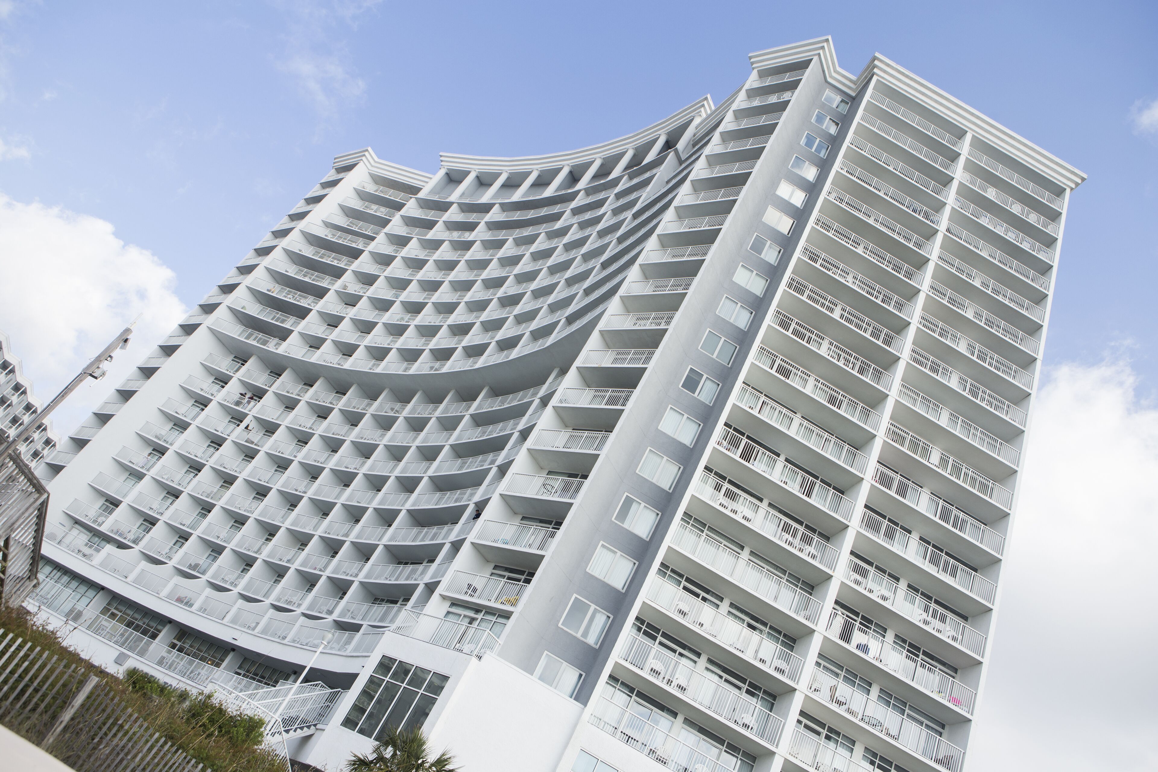 A modern high-rise building with a curved facade, multiple balconies, and a clear sky in the background.