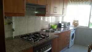 Una cocina con armarios de madera, una estufa a gas, un lavaplatos y una lavadora.