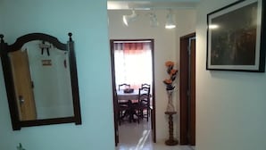 Un pasillo que conduce a un comedor con una mesa y sillas, un espejo y un jarrón con flores.