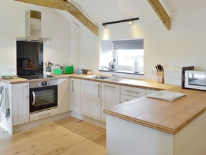 Une cuisine moderne avec des meubles blancs, un four encastré, un four à micro-ondes et un plan de travail en bois.