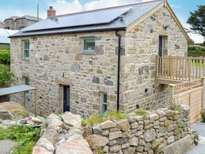 Una casa de piedra con techo inclinado, un balcón de madera y un muro de piedra en primer plano.