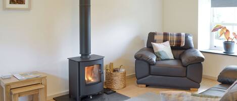 Una sala de estar acogedora con una chimenea de leña, un sofá cómodo, una pequeña mesa de madera y un ventanal con vistas.