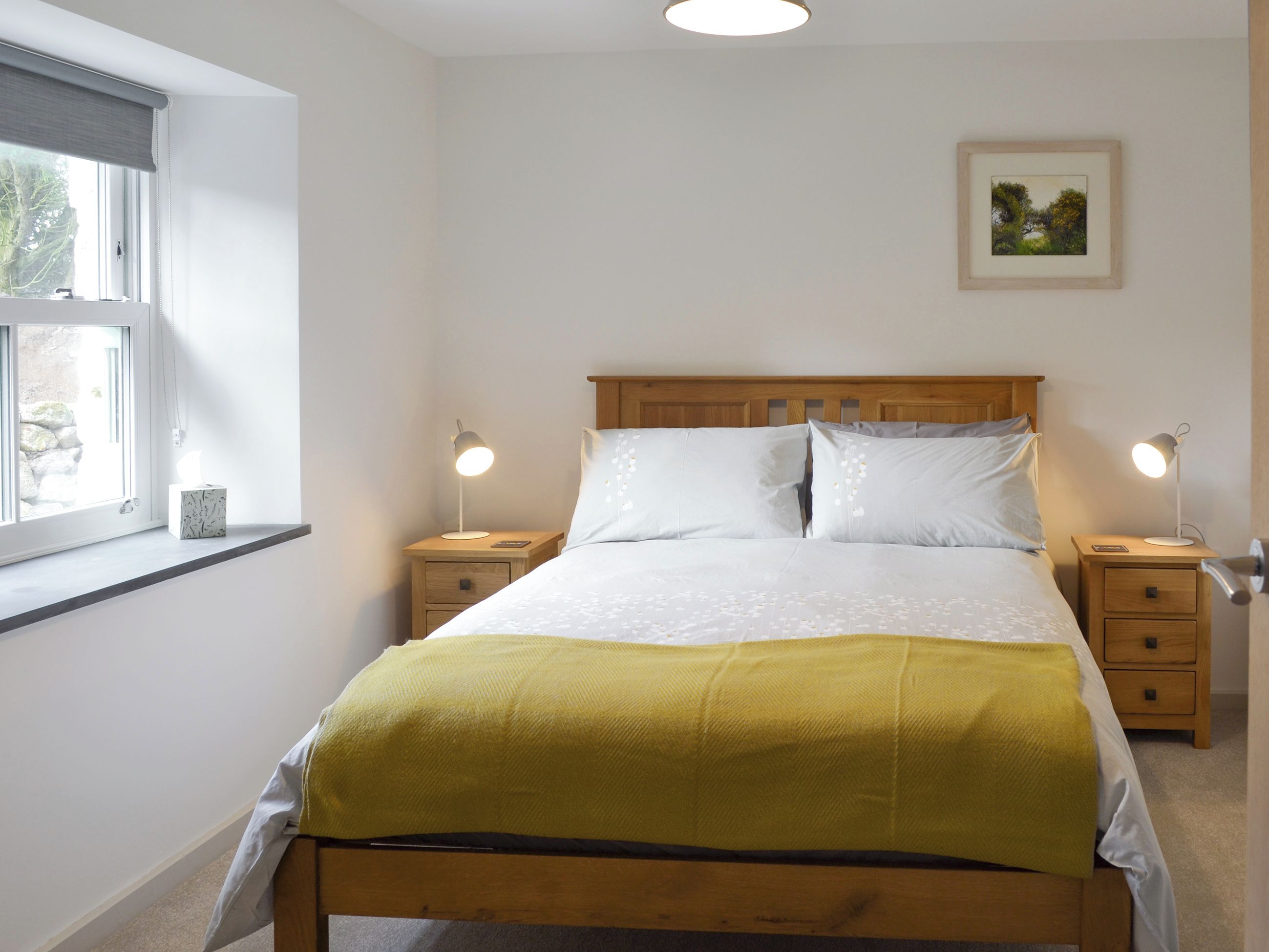 Un dormitorio con una cama, dos mesitas de noche con lámparas, un ventanal y un cuadro en la pared.