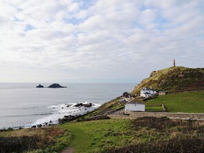 A coastal landscape with a lighthouse, grassy areas, and a small white building near the sea. - 2 bedroom accommodation in Trewellard, near St Just (Trewellard, near St Just)