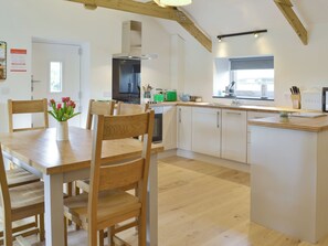 A modern kitchen with wooden cabinets, a central island, and a dining area with chairs and a table. - 2 bedroom accommodation in Trewellard, near St Just (Trewellard, near St Just)