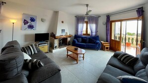 Ein Wohnzimmer mit Kamin, einem blauen Sofa, einem grauen Sofa, einem Fernseher und einem Deckenventilator.