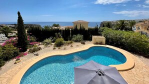 Ein Pool mit Blick auf das Meer, umgeben von viel Grün und blauem Himmel.