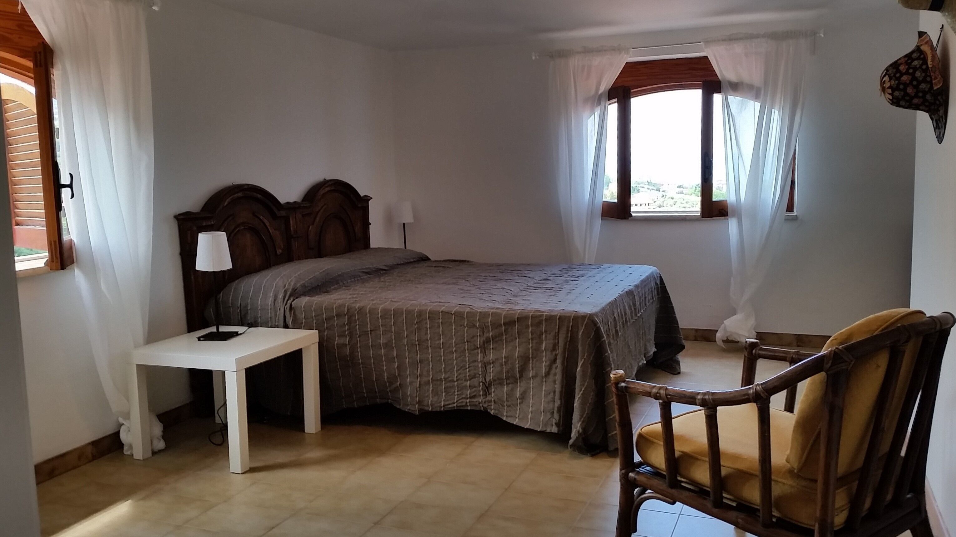 Un dormitorio con cama, mesita de noche, una silla y una ventana con cortinas.