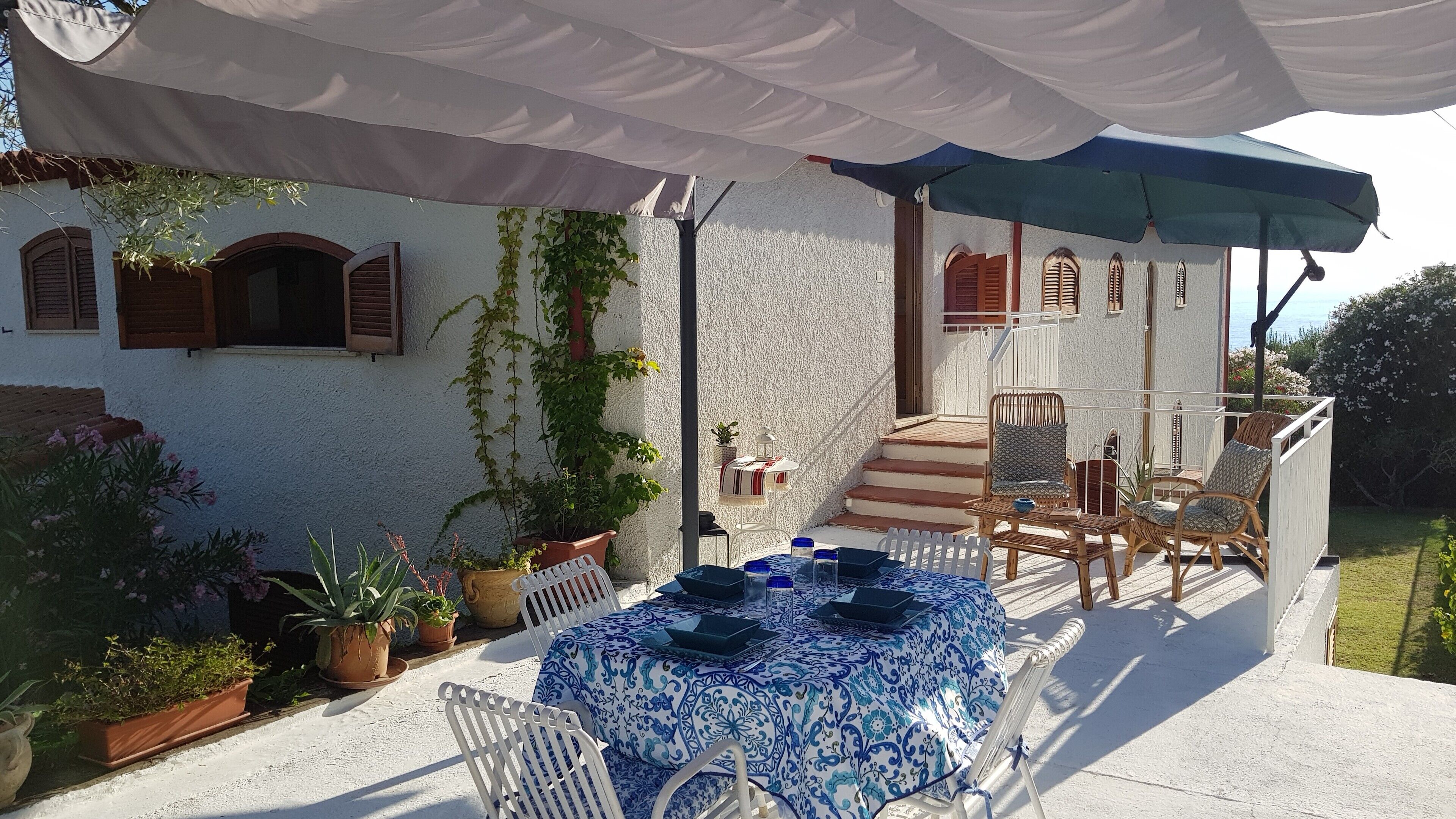 An outdoor patio with a round table set for dining, surrounded by wicker chairs.