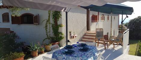 An outdoor patio with a round table set for dining, surrounded by wicker chairs.