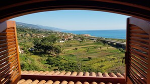 A view from a balcony with a wooden railing, overlooking a coastal landscape with fields, a bridge, and distant mountains. - Villa Anna – Sea view attic with terrace, just minutes from the beach (Fuscaldo Marina)