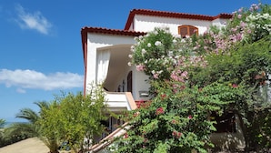 A white building with a red roof, surrounded by lush greenery and flowering plants. - Villa Anna – Sea view attic with terrace, just minutes from the beach (Fuscaldo Marina)