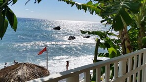 A beach view with a thatched roof structure, a flag, and a railing. - Villa Anna – Sea view attic with terrace, just minutes from the beach (Fuscaldo Marina)
