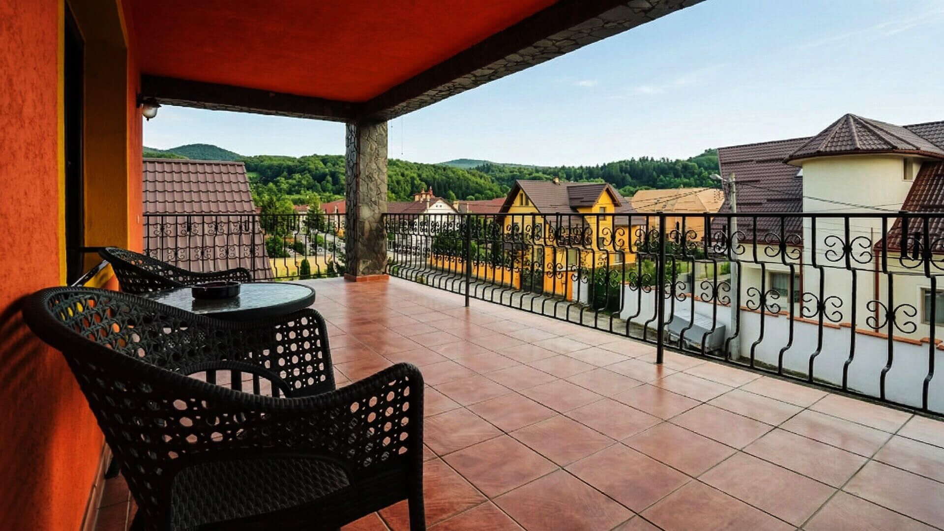 A balcony with outdoor furniture, a view of a residential area, and a stone wall.