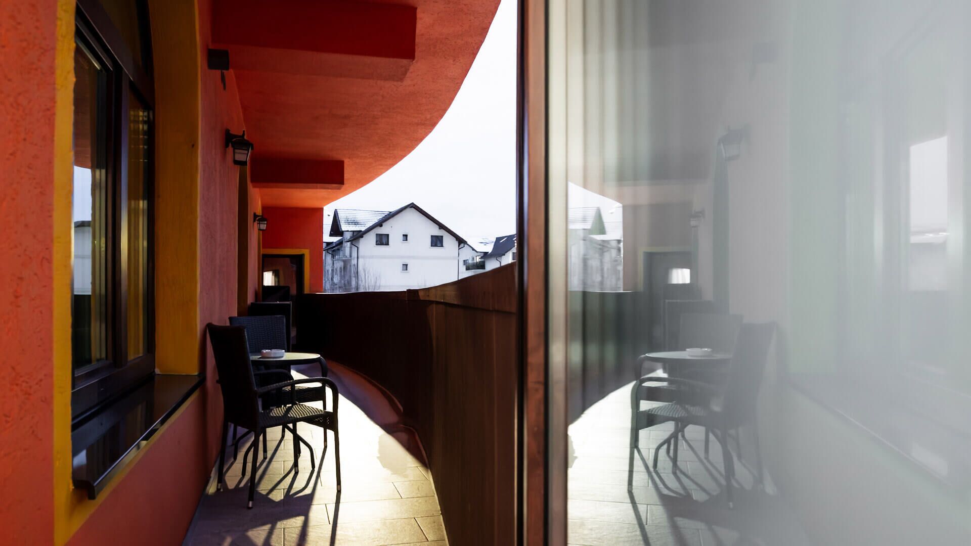 Un balcón con sillas, una mesa y una ventana, y vistas a edificios.