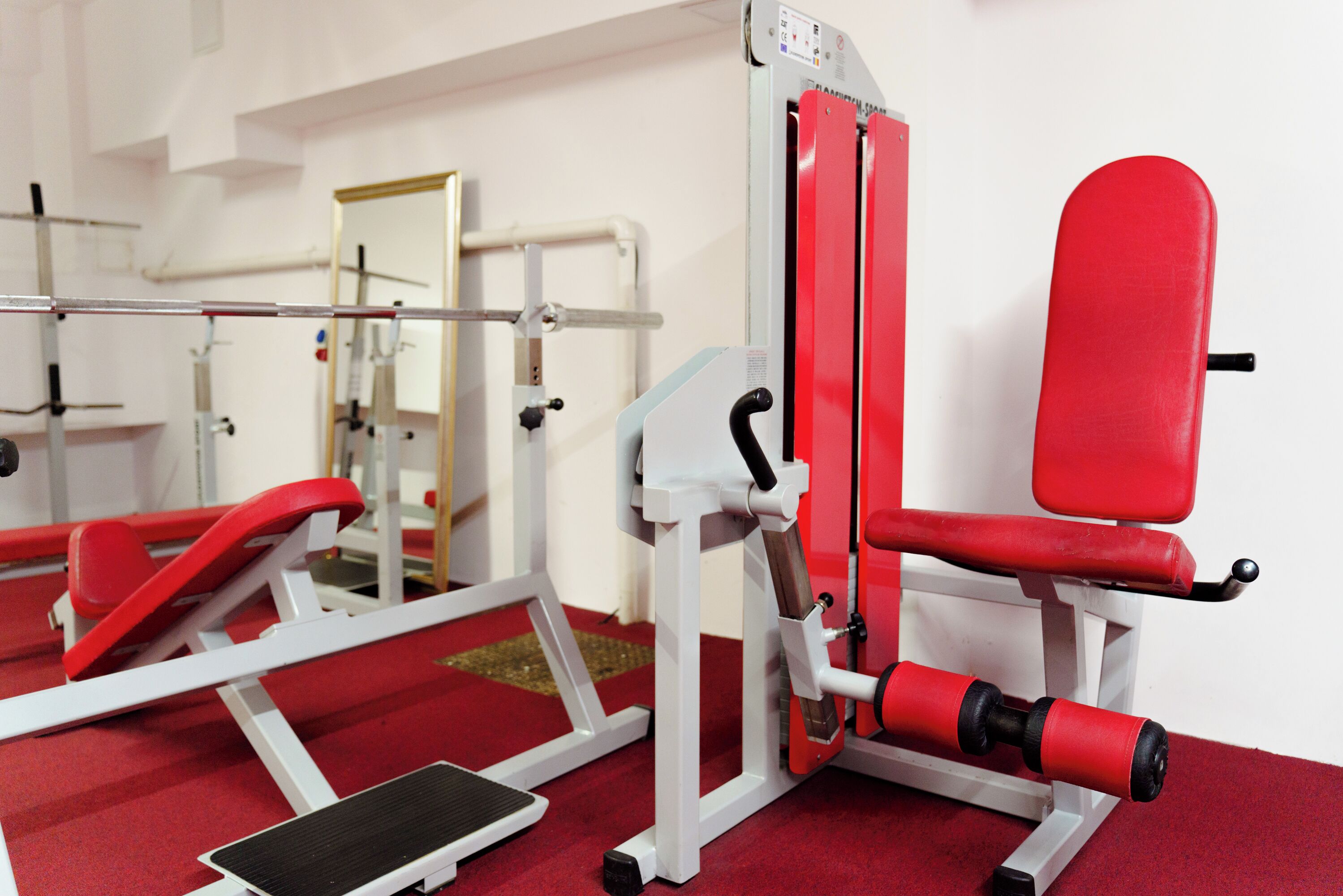 A gym with red and white exercise equipment, including a leg press machine and a bench.