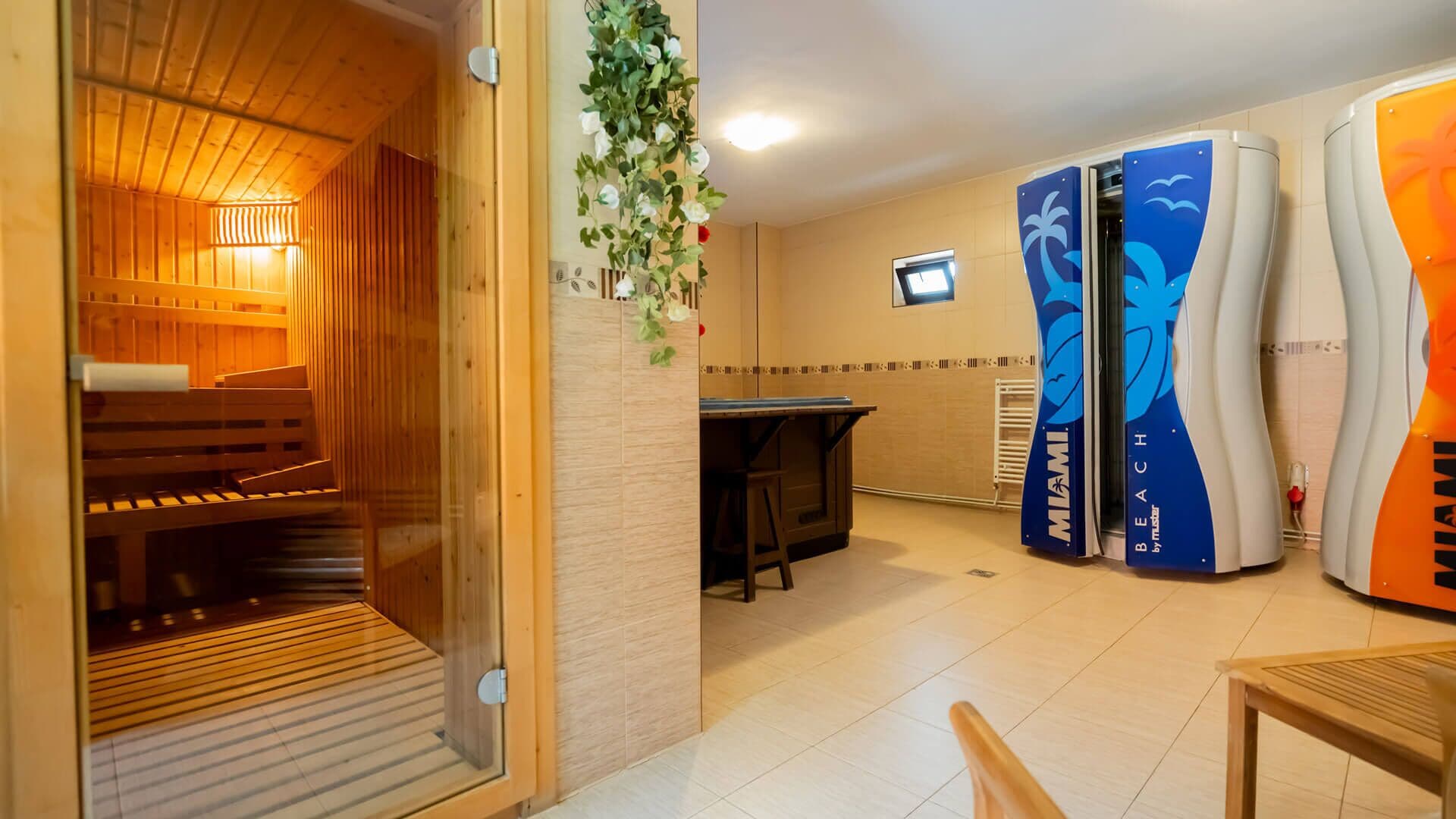 A sauna room with wooden benches and a glass door, a small table, and a wall-mounted TV.