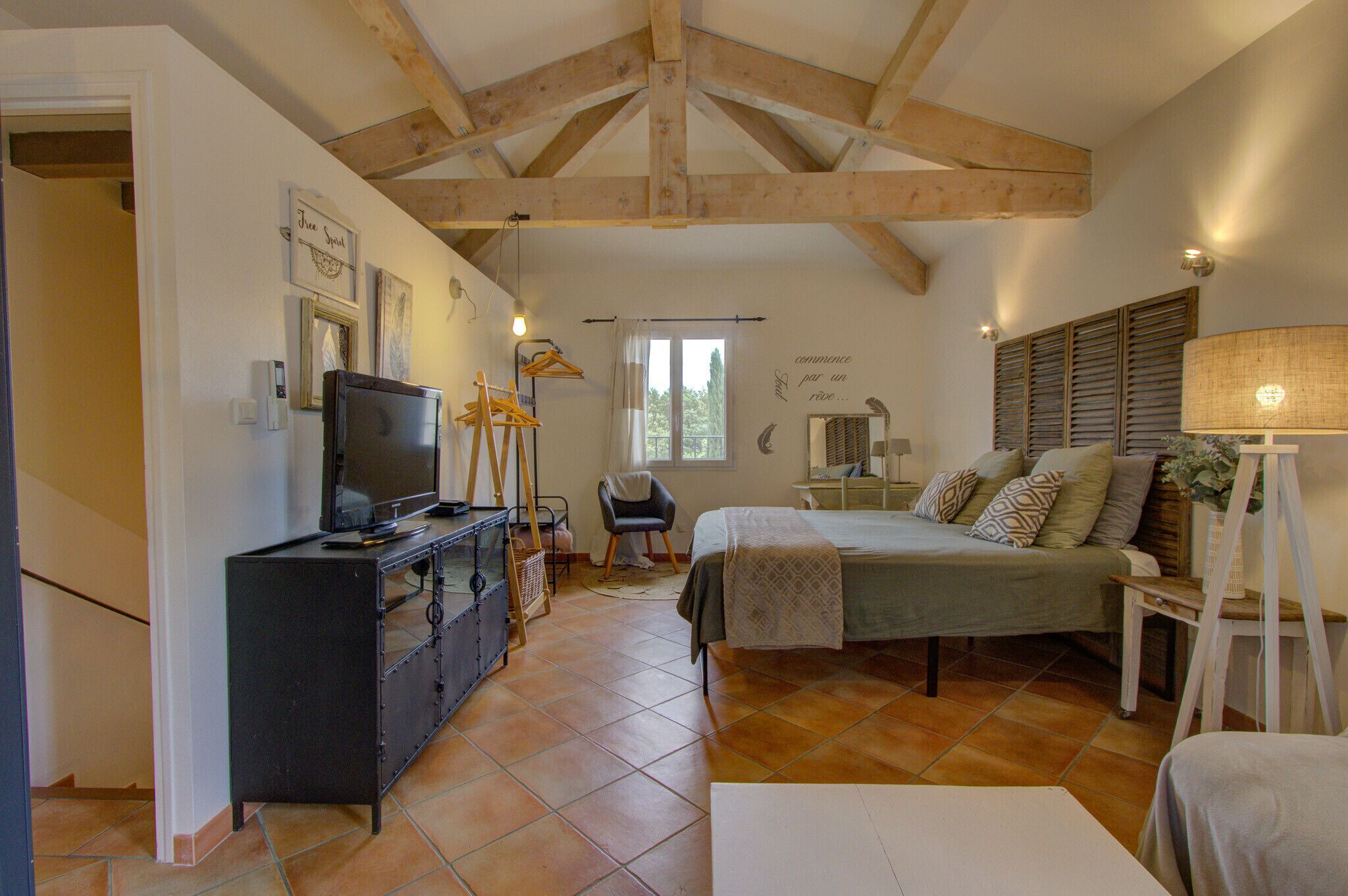 Een slaapkamer met een bed, een kast, een televisie en een raam met luiken.