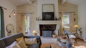 A cozy living room with a stone wall, fireplace, comfortable seating, and a clock.