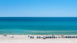 Une plage avec une eau d’un bleu limpide, du sable blanc et plusieurs parasols.