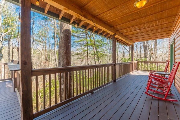 Une terrasse en bois couverte, dotée d’une rambarde, d’un banc et d’une chaise berçante.