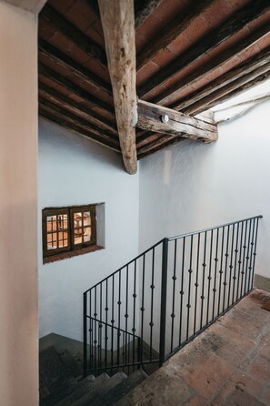 A staircase with a wooden beam ceiling, a small window, and a metal railing.
