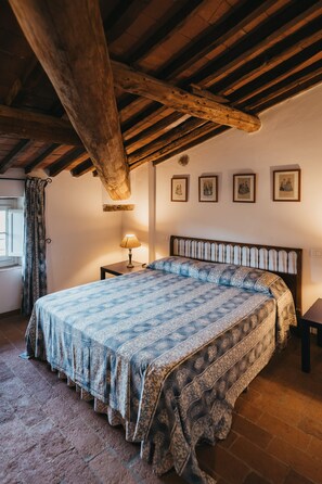 Une chambre avec un plafond en bois, un lit avec une literie à motifs, une table de chevet avec une lampe et une fenêtre avec des rideaux.