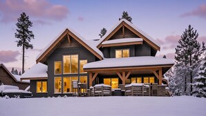 Ein großes, zweistöckiges Holzhaus mit einer überdachten Terrasse, großen Fenstern und einem mit Schnee bedeckten Dach.