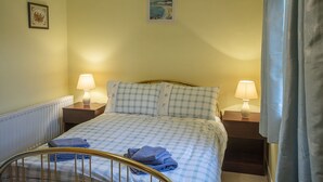 Ein ordentlich bezogenes Bett mit karierter Bettwäsche, zwei Nachttischlampen, ein gerahmtes Bild an der Wand und ein Fenster mit Vorhängen.