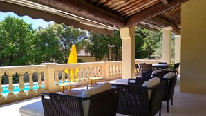A covered outdoor seating area with wicker furniture and a pool in the background. - La Villa des Amoureux, charm in Drôme Provençale, with secured swimming pool (Clansayes)