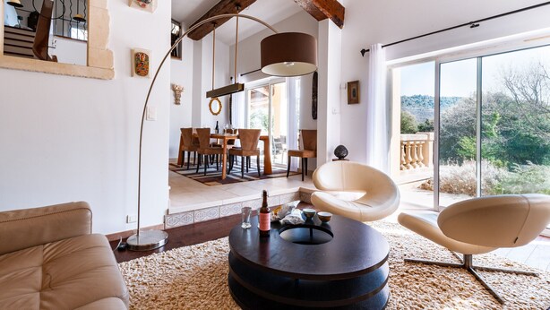 A modern living room with a round coffee table, a beige sofa, and a white chair. There is a dining area in the background with a table and chairs. - La Villa des Amoureux, charm in Drôme Provençale, with secured swimming pool (Clansayes)