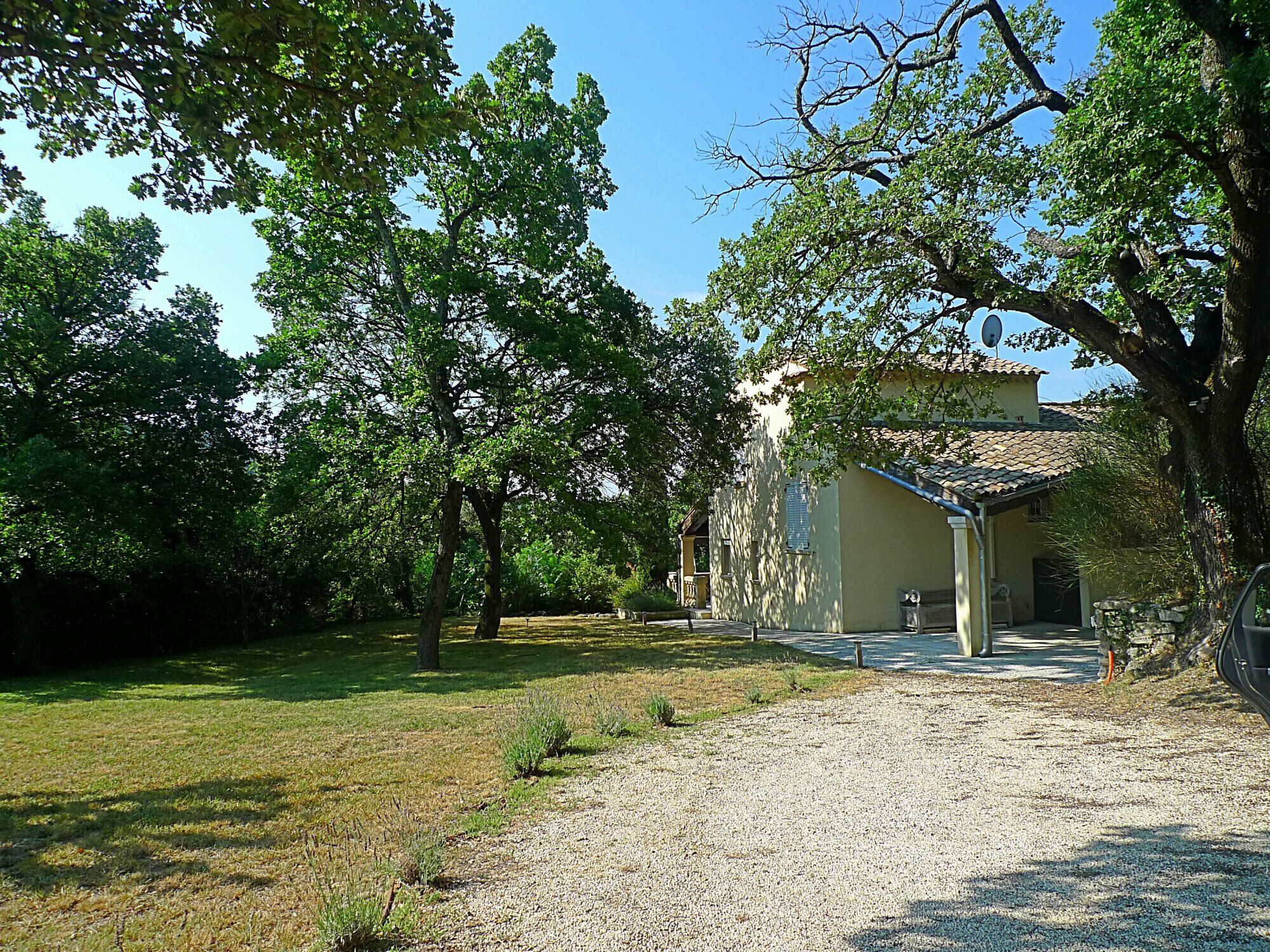 A house with a gravel driveway, surrounded by trees and a grassy area.