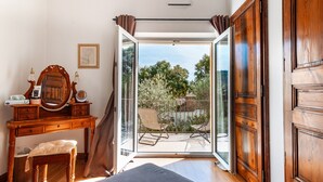 A bedroom with a wooden desk, a chair, a bed, and a sliding glass door leading to a balcony with outdoor furniture. - La Villa des Amoureux, charm in Drôme Provençale, with secured swimming pool (Clansayes)