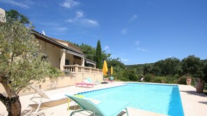 A swimming pool with lounge chairs and umbrellas, surrounded by a building and trees. - La Villa des Amoureux, charm in Drôme Provençale, with secured swimming pool (Clansayes)