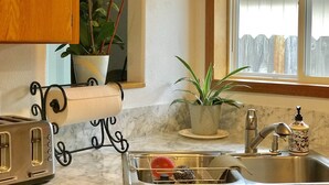 A kitchen with a marble countertop, a toaster, a sink, a window with a view of a wooden fence, and two potted plants. - Quiet, comfortable home. Near Intel and Nike campuses. (Hillsboro)