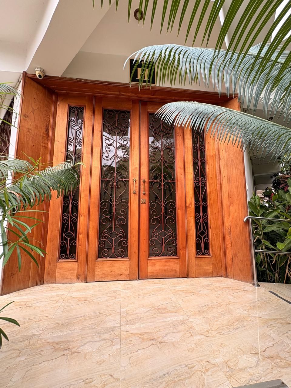 Una puerta de madera con ornamentación metálica detallada, suelo de baldosas y techo con tragaluces.