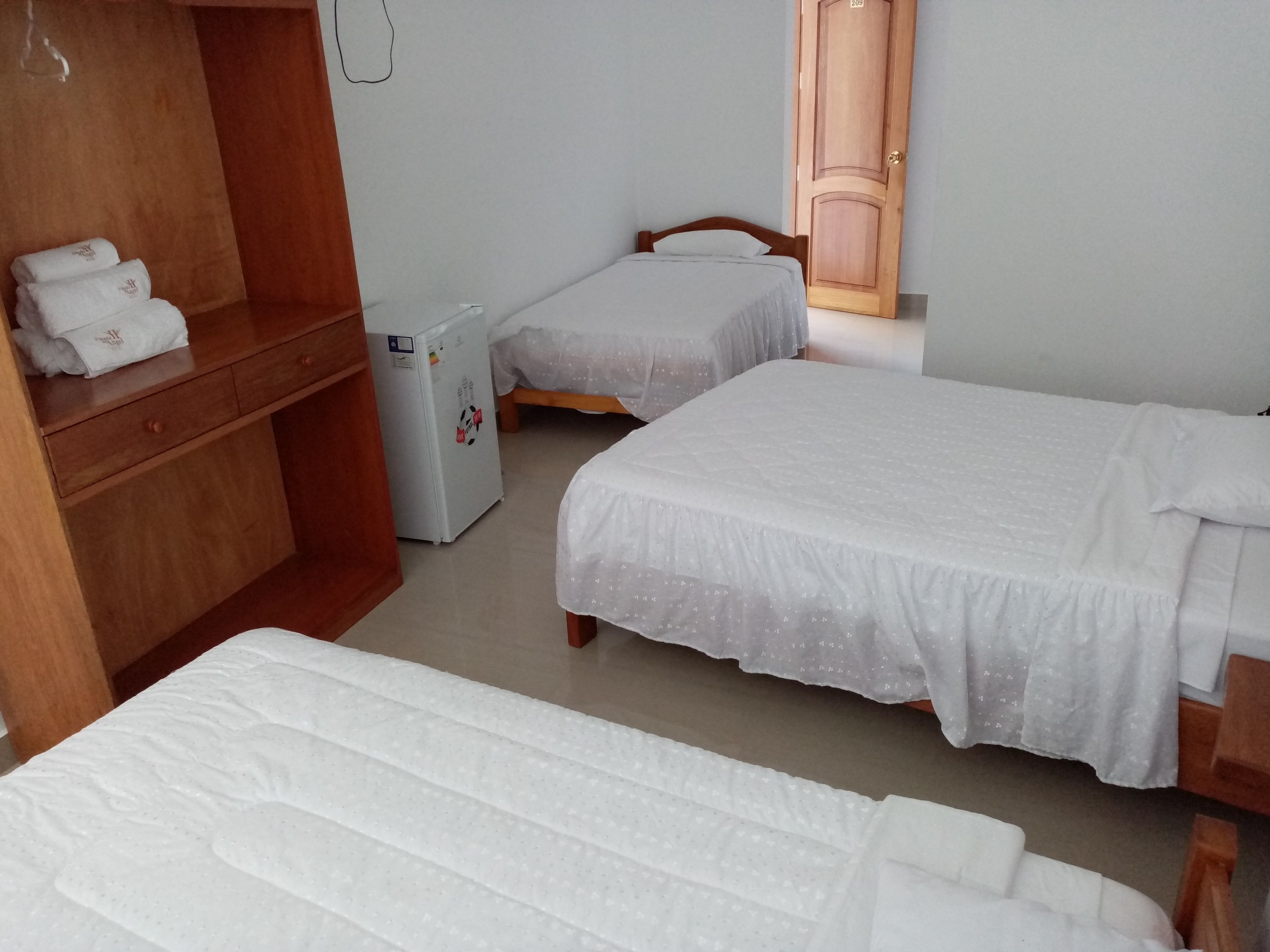 A hotel room with two single beds, a wooden wardrobe, a small refrigerator, and a mirror on the wall.